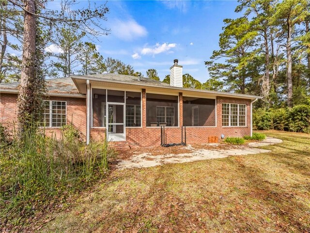 rear view of house featuring a sunroom, brick siding, a yard, and a chimney