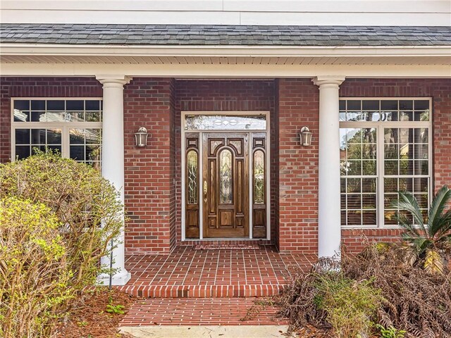 property entrance with roof with shingles and brick siding