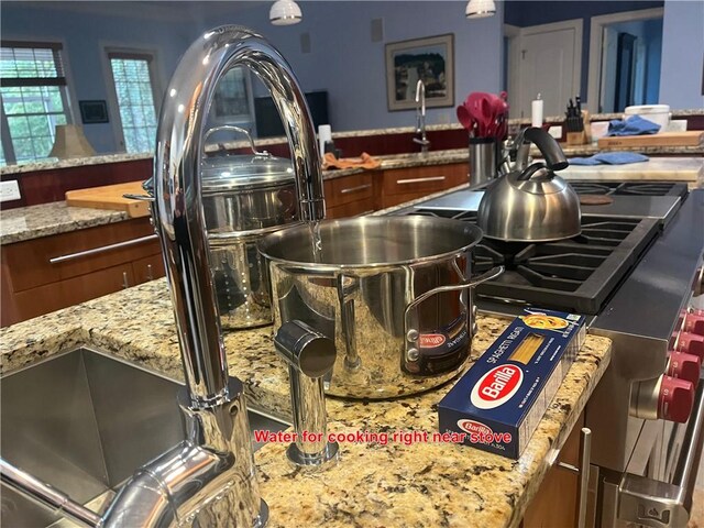 kitchen with crown molding, hanging light fixtures, a sink, and light stone countertops