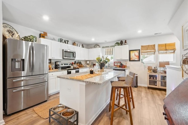 102 Cathead Ln, Darien, GA 31305 - kitchen with light wood finished floors, a breakfast bar, white cabinets, appliances with stainless steel finishes, and a kitchen island