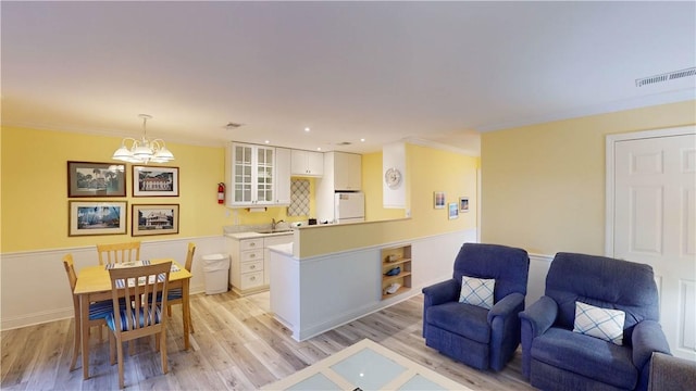 kitchen with hanging light fixtures, crown molding, a chandelier, white cabinets, and light wood-type flooring