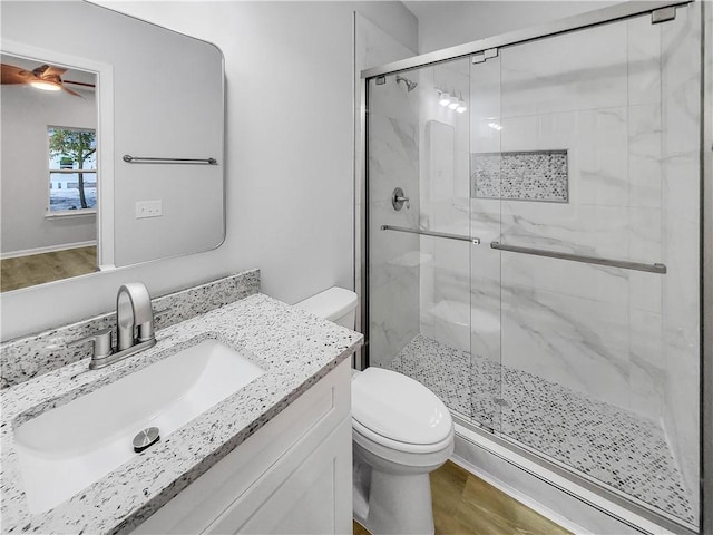 bathroom with a shower with shower door, wood-type flooring, vanity, ceiling fan, and toilet