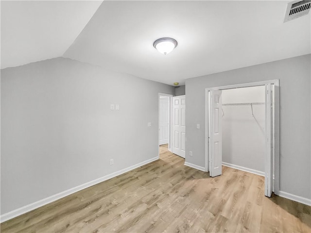 unfurnished bedroom featuring vaulted ceiling, a closet, and light wood-type flooring