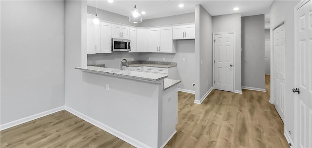 kitchen featuring sink, white cabinets, kitchen peninsula, light stone countertops, and light wood-type flooring