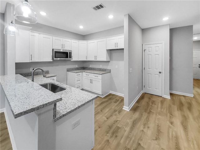 kitchen with white cabinetry, sink, light stone countertops, and hanging light fixtures