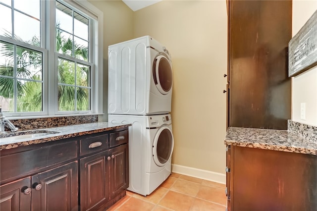 clothes washing area with stacked washer and dryer, sink, light tile patterned floors, and cabinets