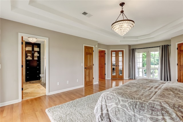 bedroom featuring an inviting chandelier, hardwood / wood-style floors, a tray ceiling, and french doors