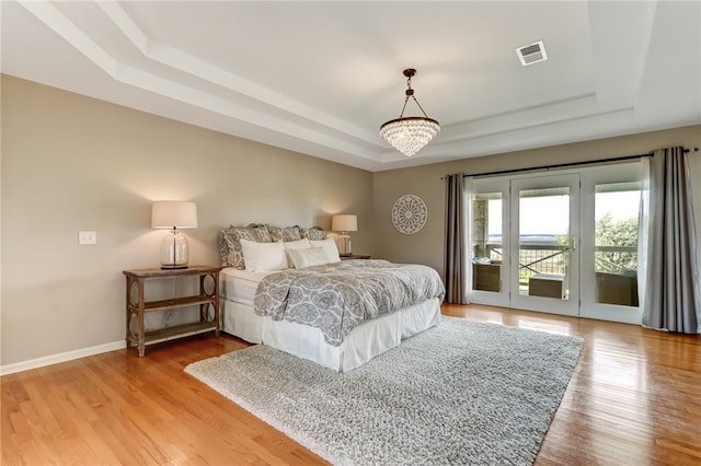 bedroom with a raised ceiling, access to exterior, a chandelier, and light hardwood / wood-style flooring