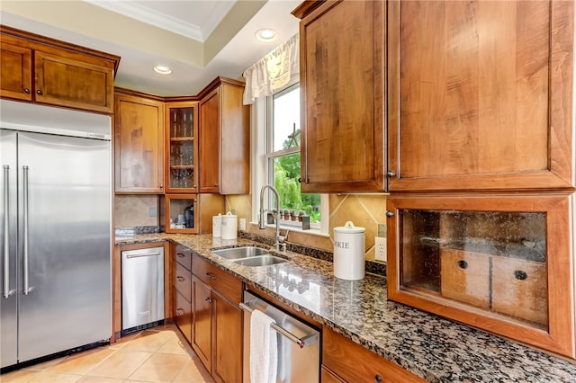 kitchen featuring sink, light tile patterned floors, dark stone countertops, ornamental molding, and appliances with stainless steel finishes