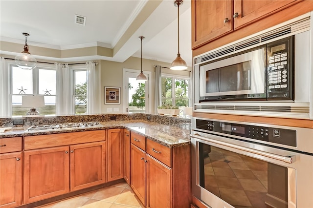 kitchen featuring pendant lighting, ornamental molding, dark stone counters, and appliances with stainless steel finishes