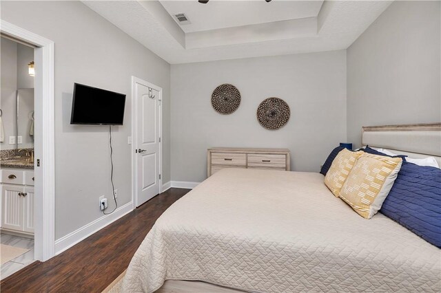 bedroom featuring a raised ceiling, dark wood-type flooring, and ensuite bath