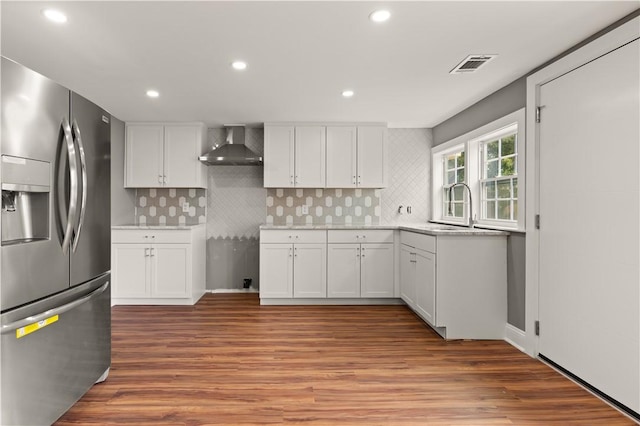 kitchen with stainless steel fridge, wall chimney exhaust hood, sink, hardwood / wood-style flooring, and white cabinets