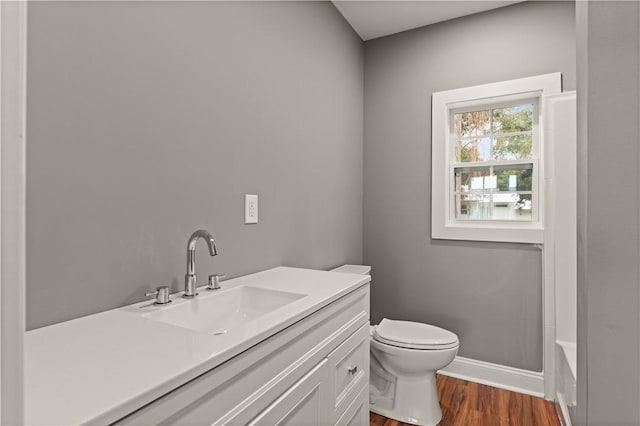 bathroom with a bath, hardwood / wood-style floors, vanity, and toilet