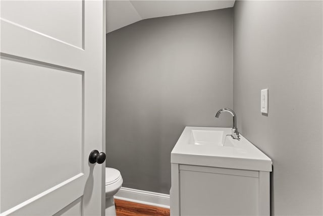 bathroom featuring hardwood / wood-style floors, vanity, lofted ceiling, and toilet