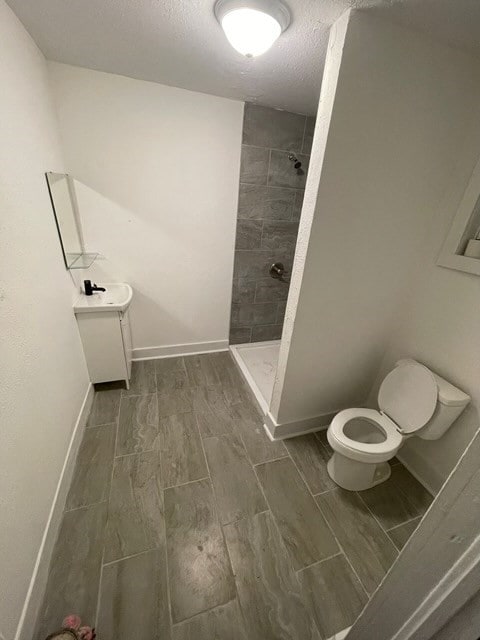 322 Archer St, Waycross, GA 31501 - bathroom with toilet, tiled shower, a textured ceiling, wood finish floors, and baseboards