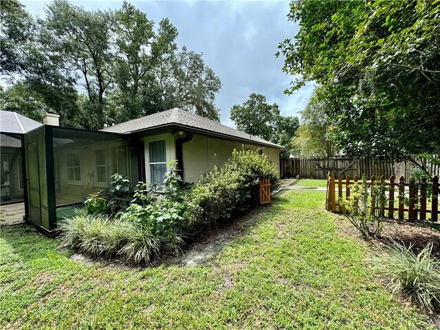 view of side of property featuring glass enclosure, a chimney, fence, and a lawn