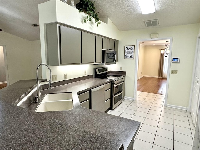 kitchen with light tile patterned flooring, gray cabinetry, a sink, appliances with stainless steel finishes, and dark countertops