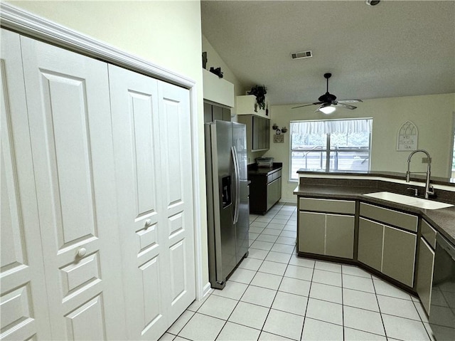 kitchen featuring light tile patterned floors, lofted ceiling, a sink, dark countertops, and stainless steel fridge