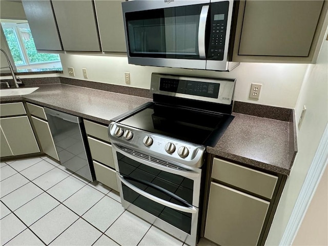 kitchen with light tile patterned floors, appliances with stainless steel finishes, dark countertops, and a sink