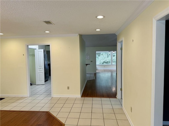 hallway with crown molding, a textured ceiling, baseboards, and light tile patterned floors