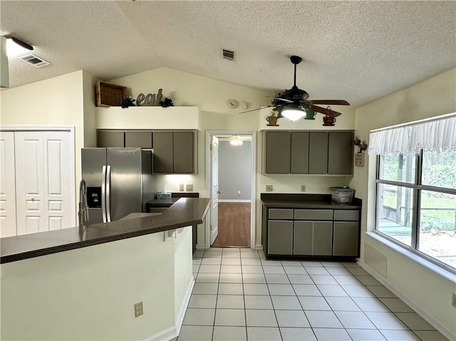 kitchen with light tile patterned floors, visible vents, dark countertops, vaulted ceiling, and stainless steel refrigerator with ice dispenser