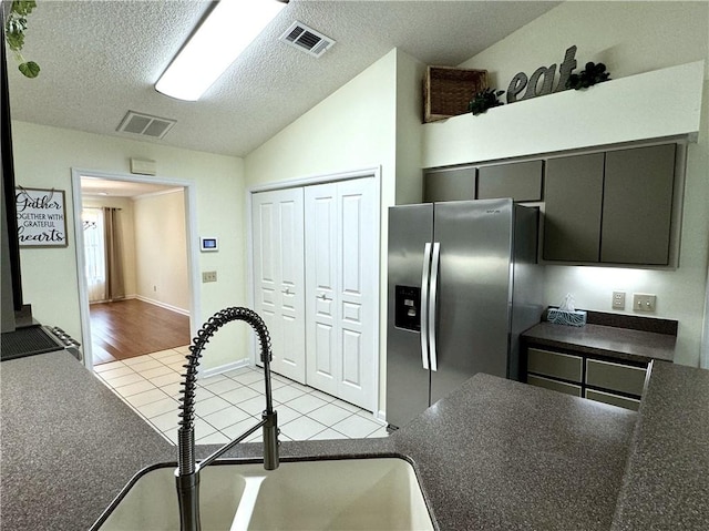 kitchen featuring dark countertops, visible vents, vaulted ceiling, a sink, and stainless steel fridge