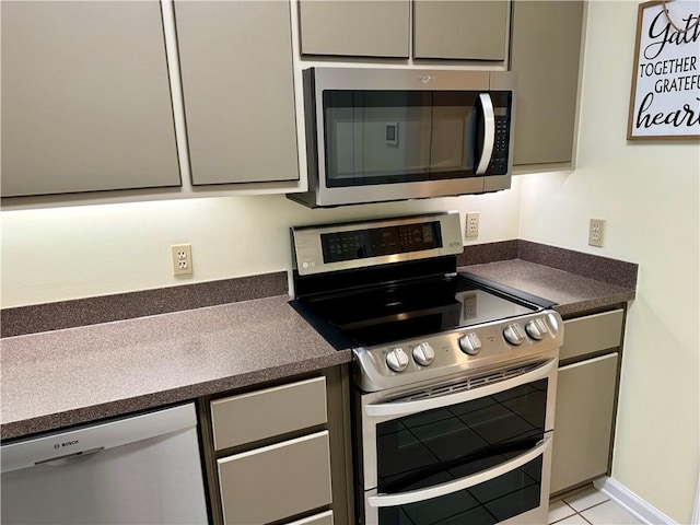 kitchen featuring light tile patterned floors, appliances with stainless steel finishes, dark countertops, and gray cabinets