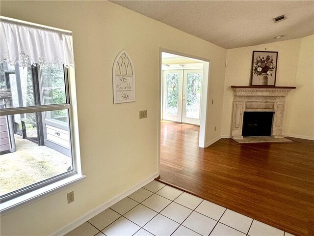 unfurnished living room with lofted ceiling, light tile patterned floors, a fireplace, visible vents, and baseboards