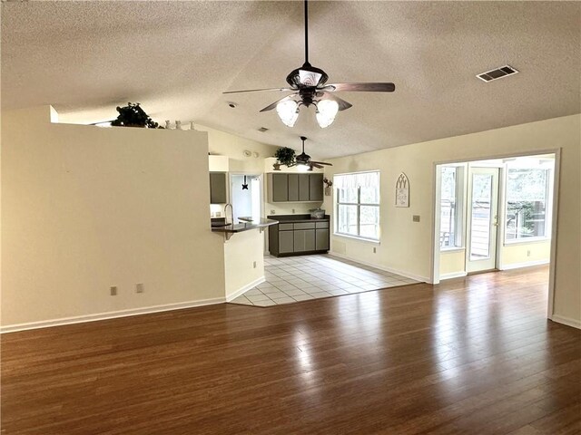 unfurnished living room featuring lofted ceiling, visible vents, light wood-style flooring, and a textured ceiling