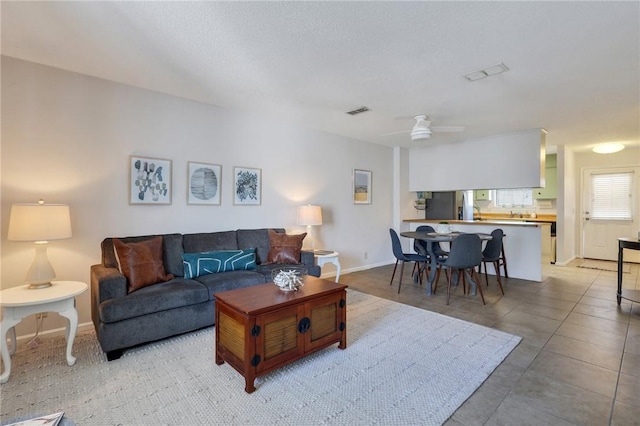 tiled living room featuring visible vents, baseboards, and a ceiling fan