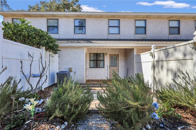 view of front facade featuring stucco siding, cooling unit, and fence