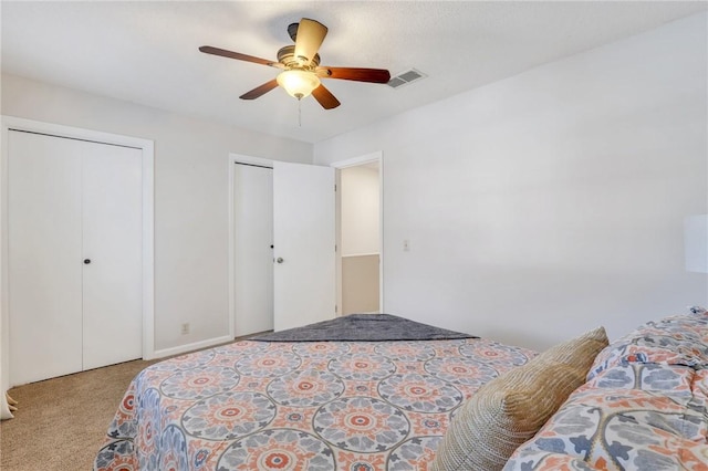 carpeted bedroom featuring visible vents, multiple closets, and ceiling fan