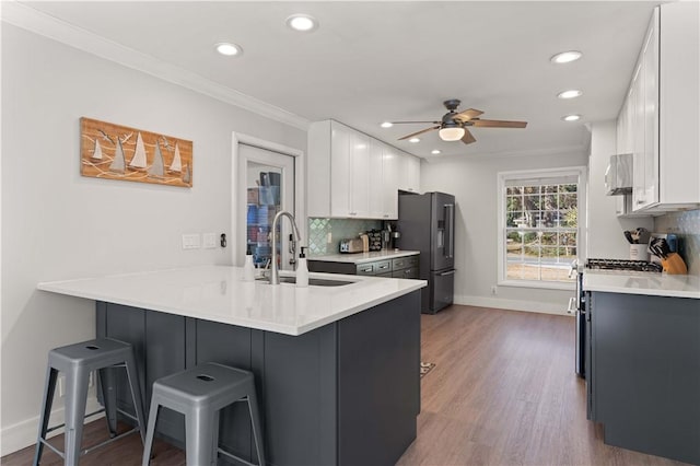 kitchen with a breakfast bar, crown molding, a sink, stainless steel fridge, and a peninsula