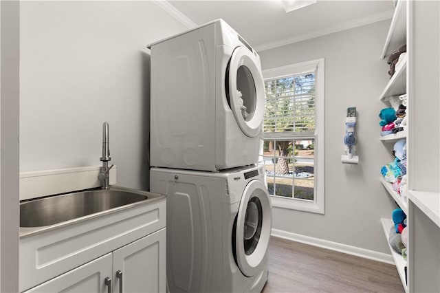 laundry room with stacked washer / dryer, a sink, cabinet space, and crown molding