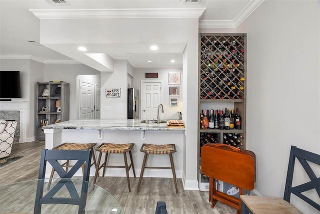 bar with stainless steel refrigerator with ice dispenser, wood-type flooring, sink, and light stone counters