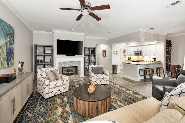 living room with dark wood-type flooring, a premium fireplace, sink, and crown molding