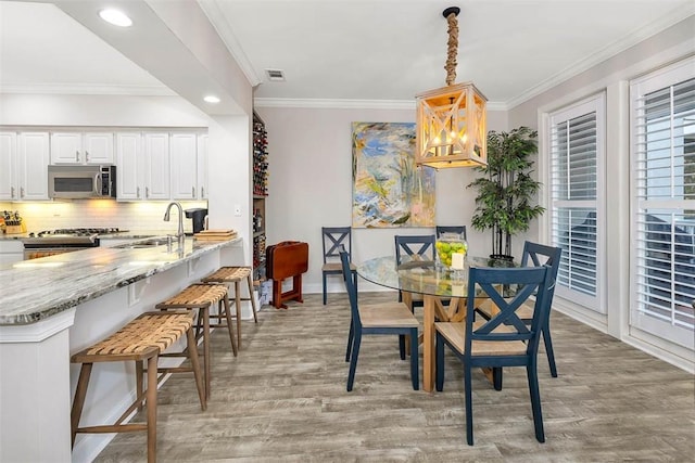 dining room with an inviting chandelier, sink, light hardwood / wood-style flooring, and ornamental molding