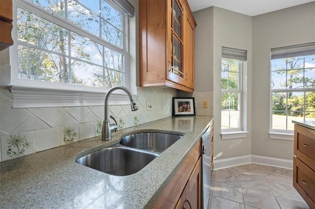 kitchen featuring backsplash, light stone countertops, sink, and stainless steel dishwasher