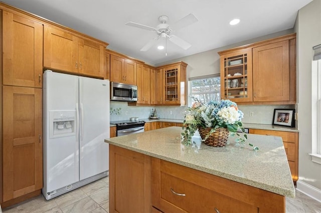 kitchen with light stone countertops, backsplash, stainless steel appliances, ceiling fan, and a kitchen island