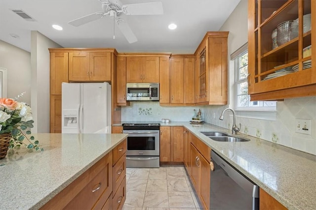 kitchen featuring ceiling fan, sink, stainless steel appliances, light stone counters, and decorative backsplash