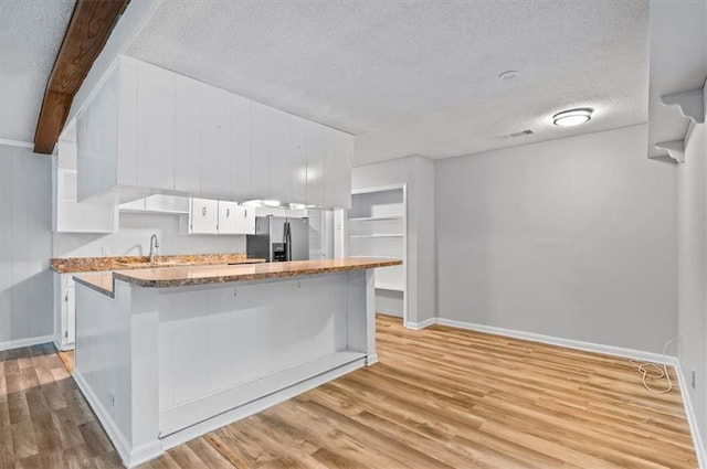 kitchen with stainless steel fridge, light wood-type flooring, a textured ceiling, beamed ceiling, and white cabinetry