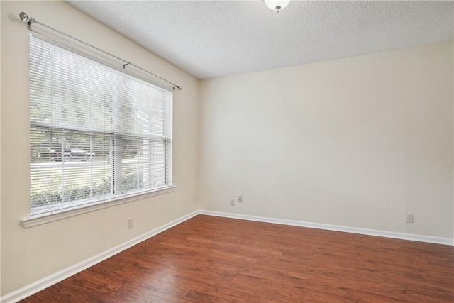 empty room with a textured ceiling, dark hardwood / wood-style floors, and plenty of natural light