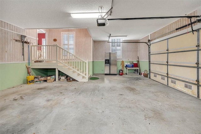 garage with wood walls, a garage door opener, and stainless steel refrigerator with ice dispenser