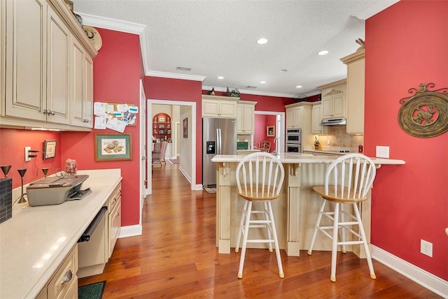 kitchen featuring appliances with stainless steel finishes, a textured ceiling, light hardwood / wood-style flooring, cream cabinetry, and a breakfast bar area