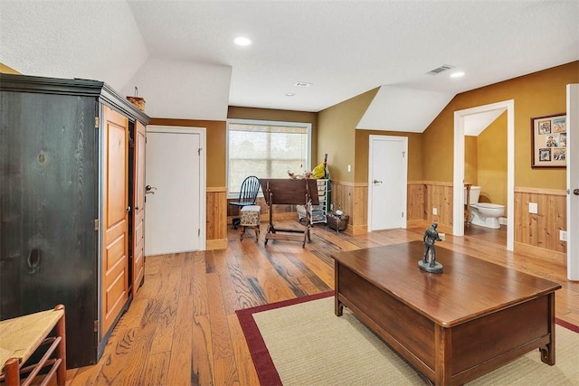 living room featuring a textured ceiling, light hardwood / wood-style floors, vaulted ceiling, and wood walls