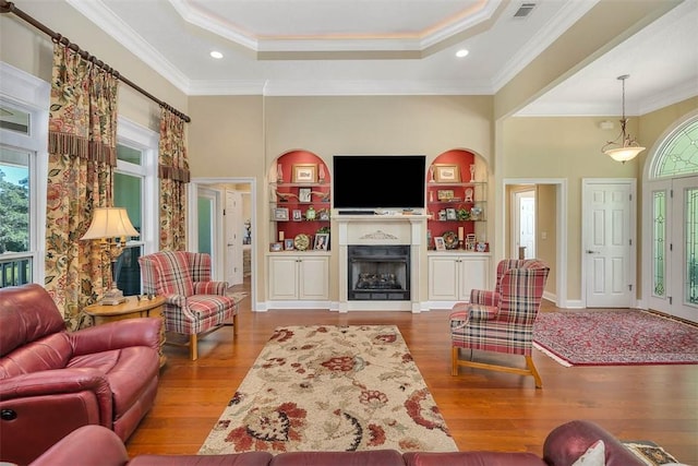 living room featuring a tray ceiling, crown molding, wood-type flooring, and a high ceiling