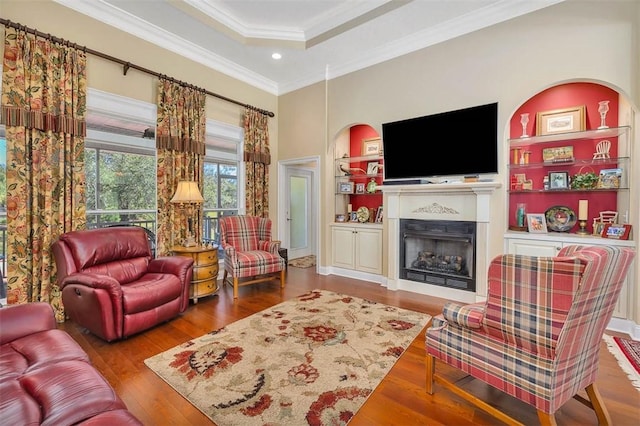 living room with built in shelves, hardwood / wood-style flooring, a tray ceiling, and ornamental molding