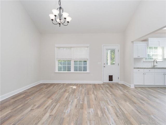 unfurnished dining area with a notable chandelier, sink, vaulted ceiling, and light wood-type flooring