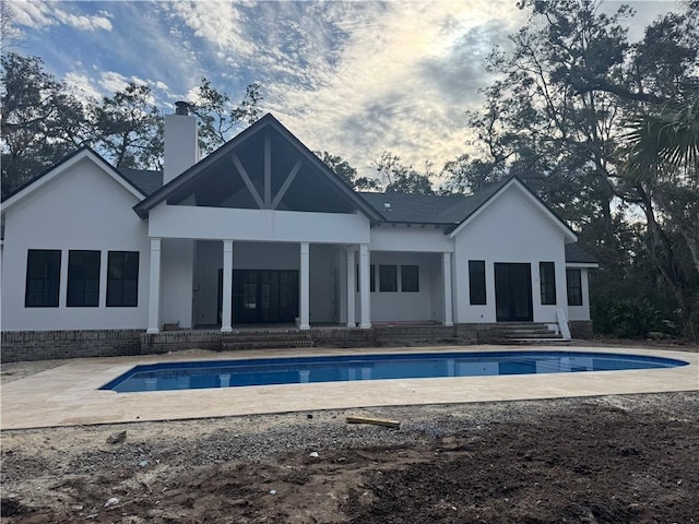 back of property featuring a patio area, an outdoor pool, a chimney, and stucco siding