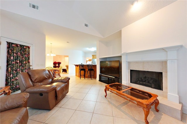 living room featuring a tiled fireplace, light tile patterned floors, high vaulted ceiling, and a notable chandelier